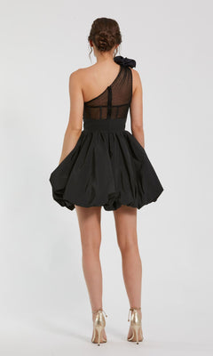 A woman faces away wearing the Mac Duggal 49858 Taffeta Short Black Party Dress, featuring a ruffled one-shoulder design, sheer panel, flared skirt, and paired with metallic high heels.