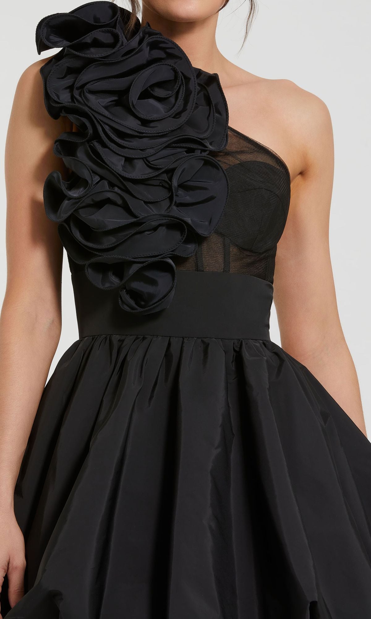 A woman wears the Mac Duggal 49858 Taffeta Short Black Party Dress with a fitted bodice and large ruffled floral detailing on the shoulder—a striking one-shoulder look, perfect for special occasions.