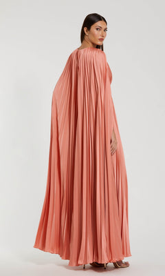 A woman stands against a plain light background wearing the Mac Duggal 49872 Cape-Sleeve Long Formal Dress in a peach hue, featuring elegant pleats and a flowing cape-like design.