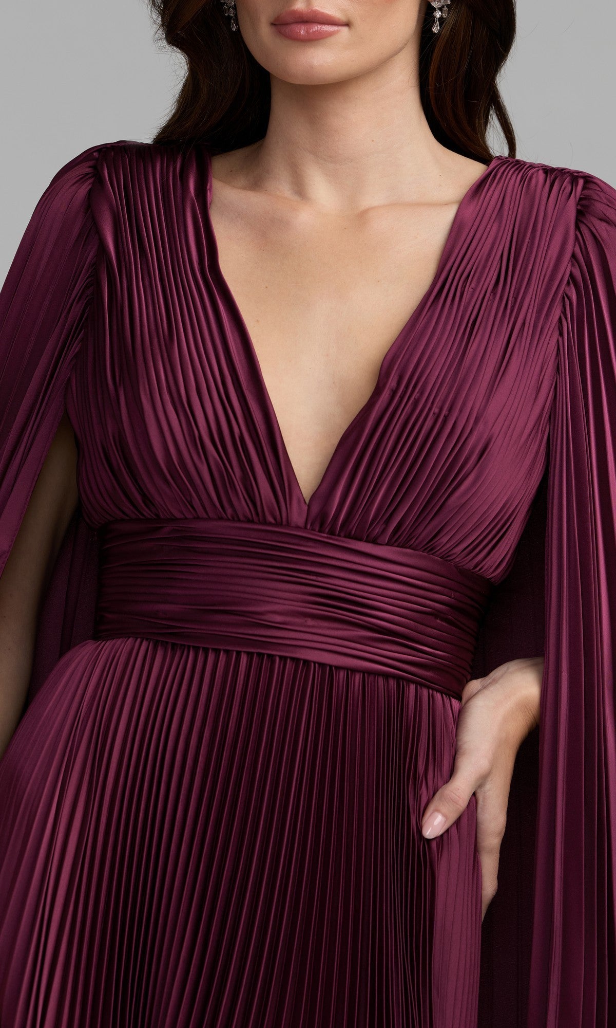 Woman wearing the Mac Duggal 49872 Cape-Sleeve Long Formal Dress in deep burgundy, featuring a pleated design, deep V-neckline, wide waistband, and cape-style sleeves.
