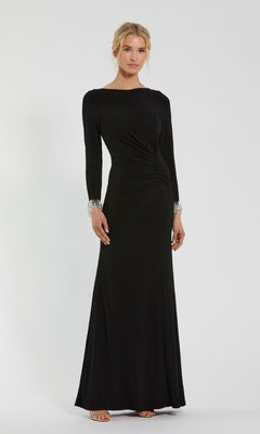 A woman stands against a plain light background wearing the Mac Duggal 49896: a long sleeve black formal dress featuring subtle waist ruching and ornamented cuffs.