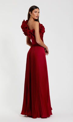 A woman models the Mac Duggal 49902 Pleated One-Shoulder Prom Gown, a floor-length, deep red dress featuring large floral details on one shoulder, against a plain white background.