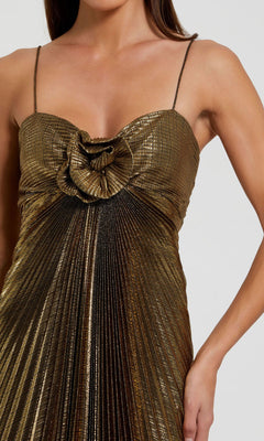 A woman wearing the Metallic Gold Long Prom Dress (Mac Duggal 49905), featuring thin straps, pleats, and a rosette detail on the bodice.