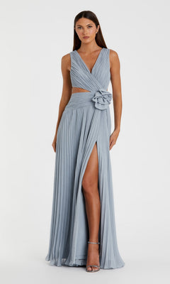 A woman stands against a plain background in the Lilac Long Pleated Formal Dress: Mac Duggal 49938, featuring a sleeveless design, high slit, side cutout, and a large flower at the waist.