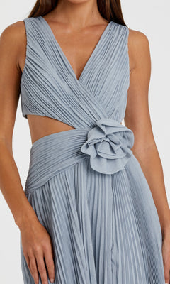 A woman in the Lilac Long Pleated Formal Dress: Mac Duggal 49938, featuring a sleeveless wrap design, v-neck, side cutout, pleats, and a bold fabric flower at the waist.