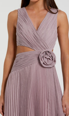 A woman wearing the Mac Duggal 49938 long formal dress, which features a sleeveless chiffon design with a V-neckline, pleated long skirt, waist cutout, and a large fabric flower accent on the skirt.