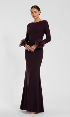 A woman in the Mac Duggal 49949 long sleeve formal dress in dark purple, featuring ruffled floral-accented sleeves, stands before a light gray backdrop.