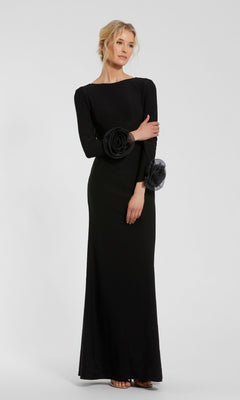 A woman stands against a plain light gray background, wearing the Mac Duggal 49949 long sleeve long formal dress with floral sleeve accents.