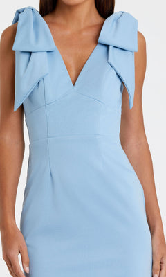 A woman wearing the Mac Duggal 49954 V-Neck Midi Wedding Guest Dress, a sleeveless light blue tea-length dress with large bows on each shoulder.