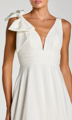 A woman wears the Shoulder-Bow Long Formal Dress by Mac Duggal 49972, featuring an elegant white A-line silhouette, sleeveless deep V-neckline, and a statement bow on one shoulder—ideal for evening occasions.