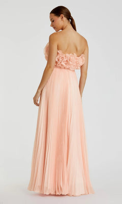 A woman wearing the Mac Duggal 49975 long formal dress in pink pleated chiffon with a strapless floral-detailed bodice stands facing away, head turned to the side.