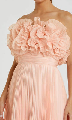 A woman wearing the Mac Duggal 49975, a strapless long formal dress in pleated peach chiffon with bold ruffled floral bodice detail—a signature style from Mac Duggal.