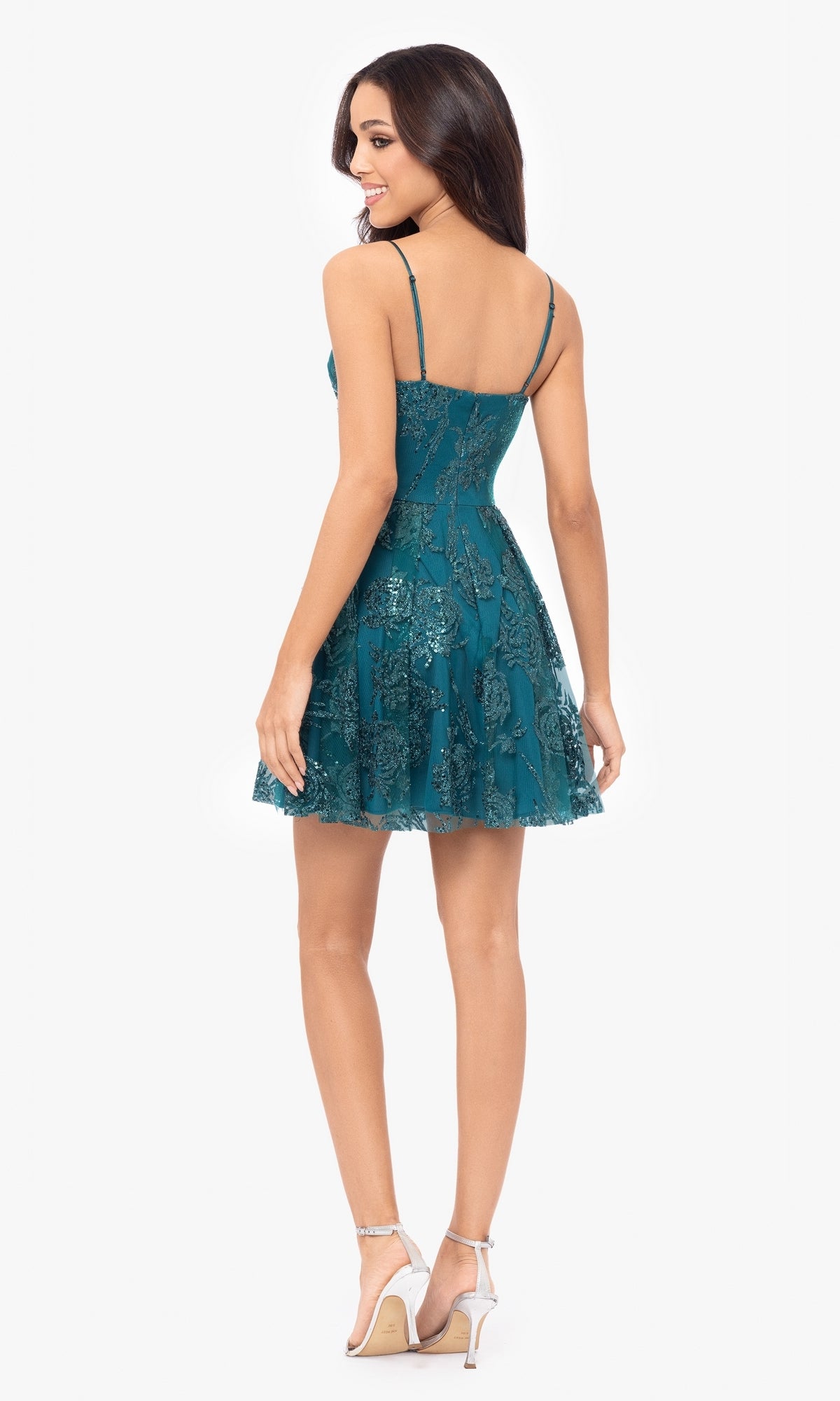 Woman in the Cut-Out Short Teal Glitter-Print Hoco Dress 4997BN with spaghetti straps, wearing heels, stands facing away and looks over her shoulder.