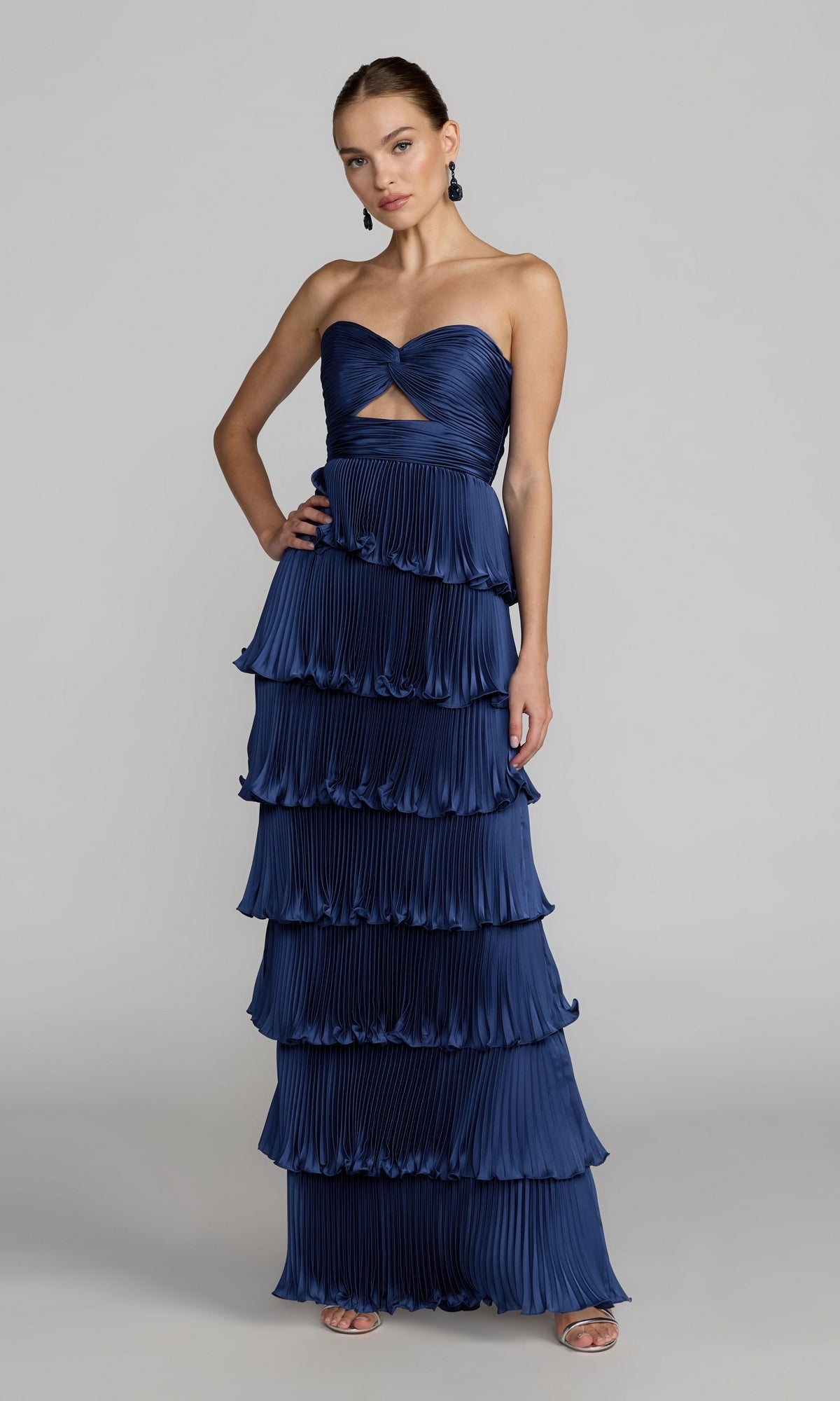A woman wearing the Mac Duggal 49981 Strapless Pleated Long Formal Dress in navy, featuring floor-length tiered ruffles, stands against a plain gray background—a stunning choice for prom.