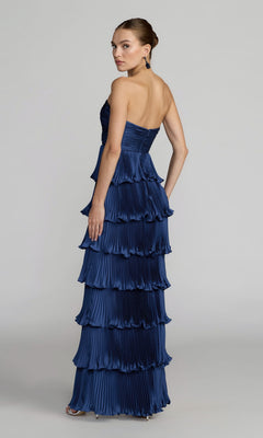 A woman poses against a plain background, looking over her shoulder in the Mac Duggal 49981 Strapless Pleated Long Formal Dress—a floor-length, navy blue gown with tiered pleats—making it a perfect choice for any special occasion.