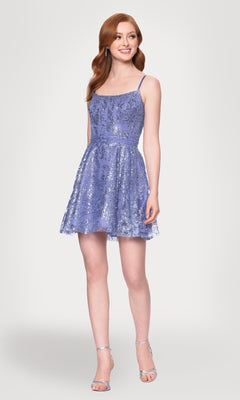 A woman smiles while wearing the Blondie Nites 5001BN-1 Mini Glitter Hoco Dress, a sleeveless, light purple cocktail dress with thin straps, paired with silver high-heeled sandals against a plain background.