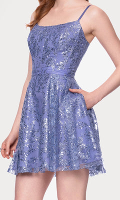 A woman models the Mini Glitter Hoco Dress: Blondie Nites 5001BN-1, a sleeveless lavender junior party dress with silver sequins, fitted bodice, flared skirt, and pockets—ideal as a glitter cocktail or short homecoming dress.
