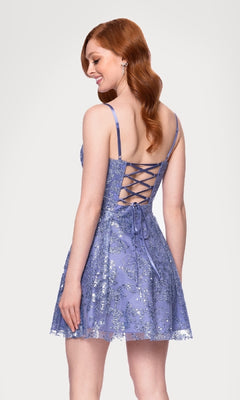 A woman with long red hair models the Blondie Nites 5001BN-1 Mini Glitter Hoco Dress—sleeveless with a lace-up back and silver floral designs—standing against a plain white background.