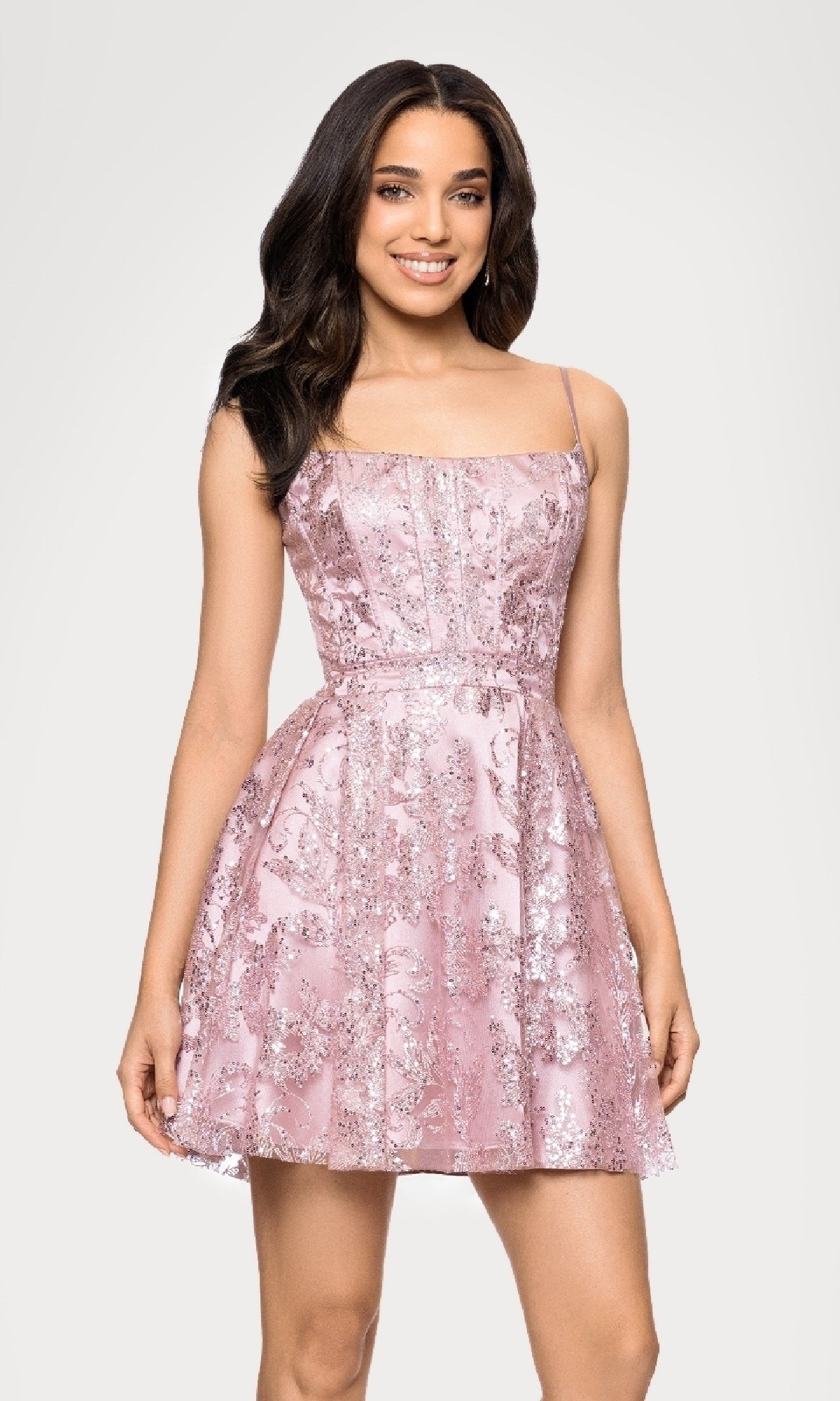 A woman smiles while wearing the Mini Glitter Hoco Dress: Blondie Nites 5001BN-1 in rose—a sleeveless sequin junior party dress with a flared skirt—standing against a plain white background.