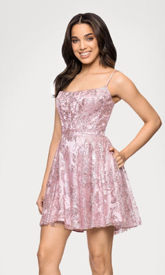 A woman smiles in the Blondie Nites 5001BN-1 Mini Glitter Hoco Dress, a short pink junior party dress with sequin details, styled like a glitter cocktail dress, set against a plain light background.