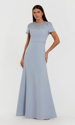 A woman wearing the Mac Duggal 50038 long formal dress in powder blue—a floor-length crepe trumpet gown adorned with bead embellishments on the bodice and featuring short sleeves—standing against a plain white background.