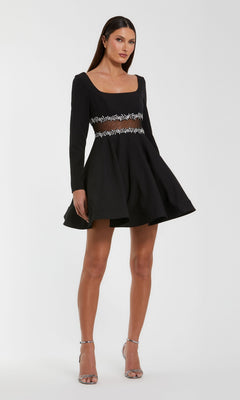 Woman wearing the Short Party Dress: Mac Duggal 50047 in black, featuring a fit-and-flare silhouette with a square neckline, beaded sheer waistline, and flared skirt, paired with silver high-heeled sandals and standing against a plain background.