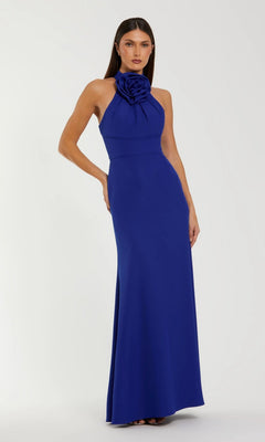 Woman in a sleeveless Mac Duggal 50053 long formal dress in cobalt, featuring a high halter neck and bold 3D rosette detail, stands against a plain light background.
