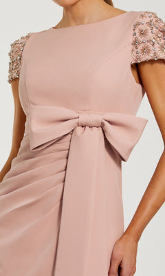 Woman wearing a green Mac Duggal 50054 formal gown with embellished short sleeves, a large front bow at the waist, and gathered fabric detail.