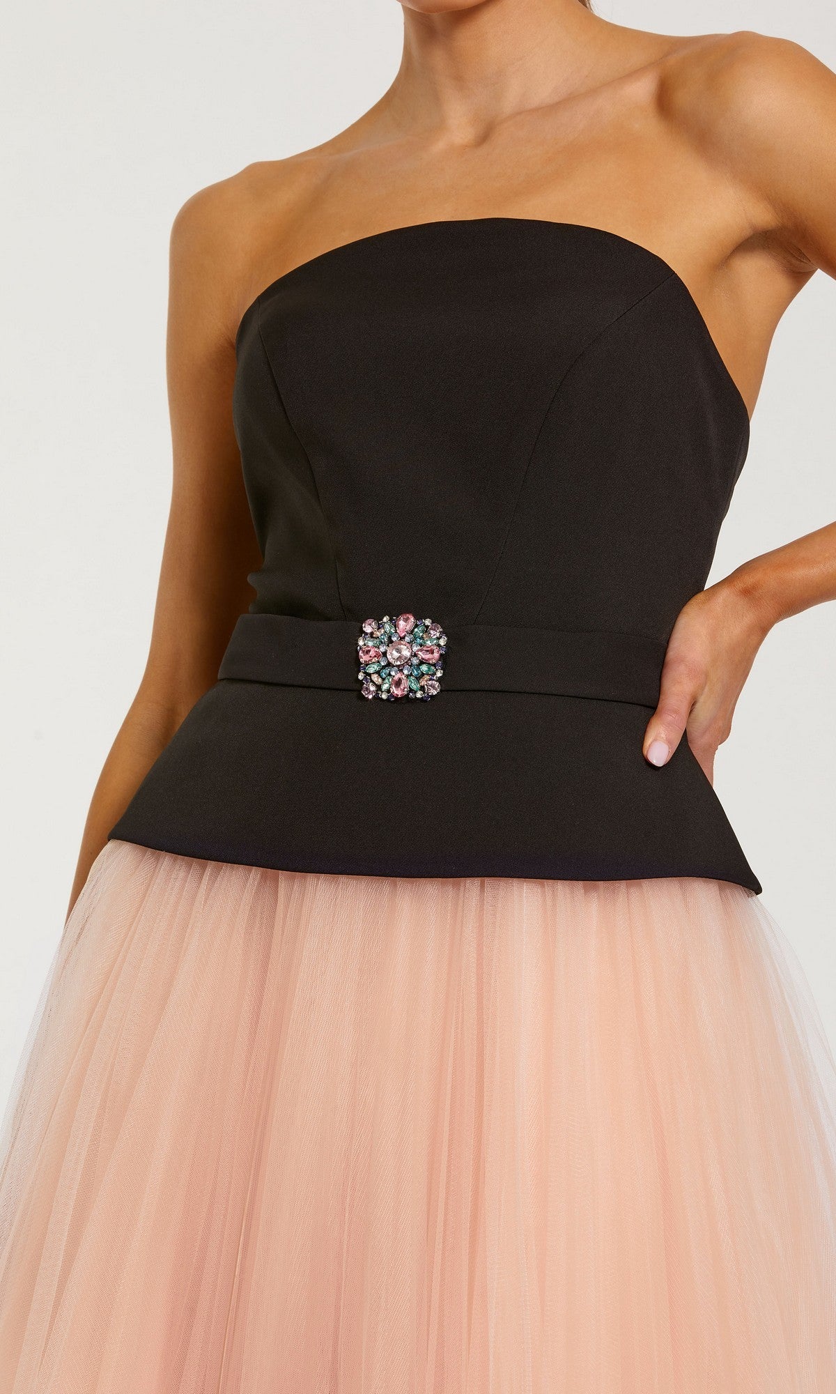 A woman wearing the Mac Duggal 50063 long formal dress, featuring a strapless black top adorned with a jeweled brooch and a pink tulle midi skirt for an elegant look.