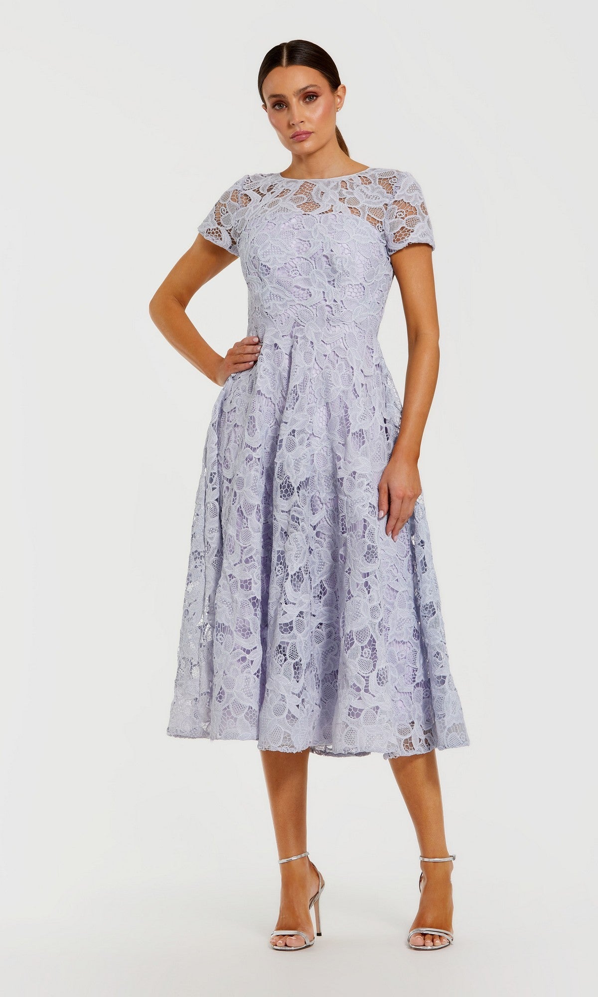 A woman wearing the Midi Party Dress: Mac Duggal 50073 in lilac, featuring floral lace, short sleeves, and an elegant a-line midi skirt, paired with high heels and standing against a plain white background.
