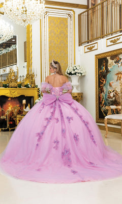 A person in the Quinceanera Dress 5007 By Dancing Queen, featuring a lavish pink corset bodice, stands facing away in an ornate room adorned with gold accents, a fireplace, chandeliers, and large framed artwork.