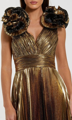 A woman wears the Mac Duggal 50084 long formal dress, a pleated sleeveless metallic gold gown featuring large ruffled black and gold floral shoulder accents.