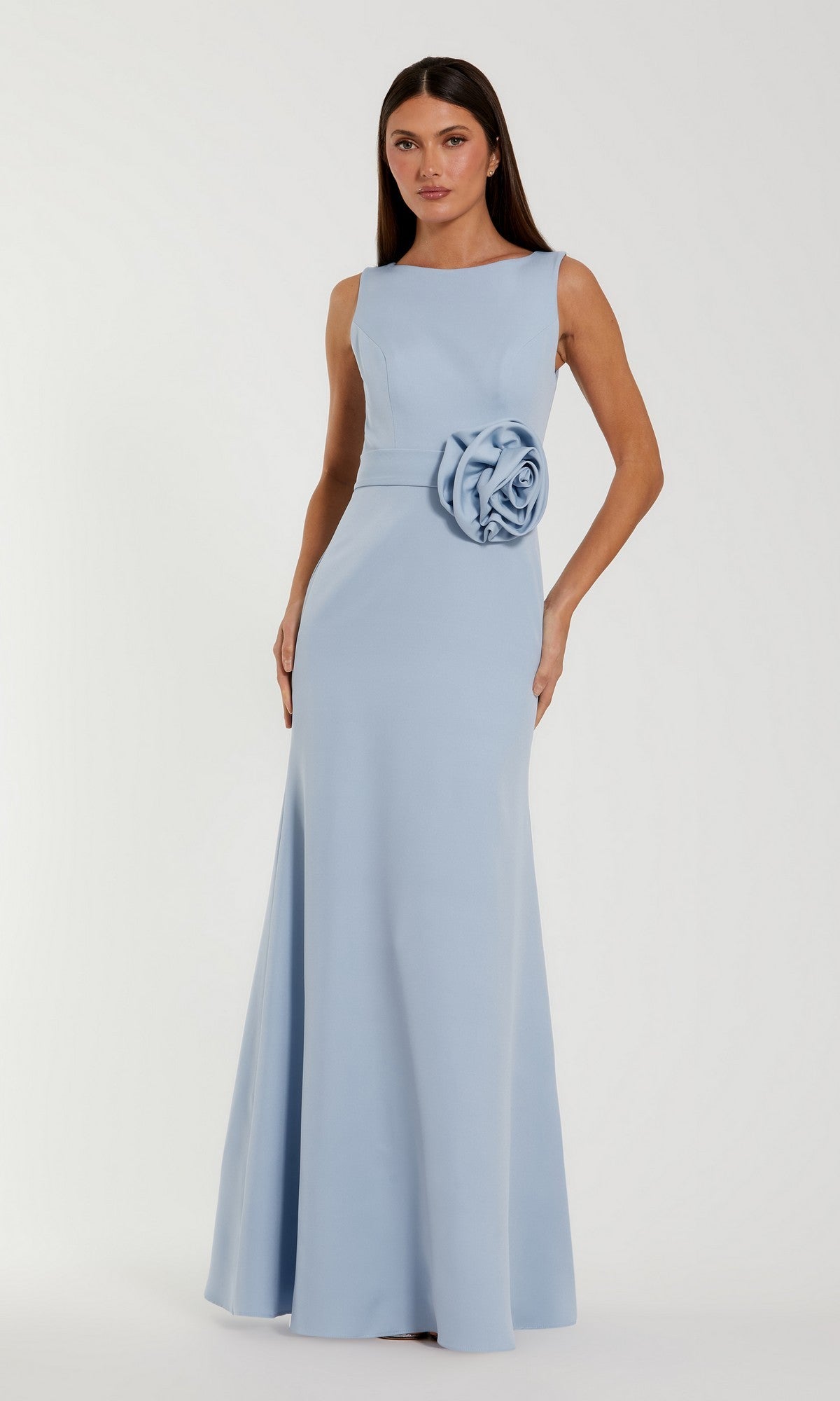 A woman wears the Mac Duggal 50097 long formal dress in periwinkle—a floor-length, sleeveless crepe gown featuring a striking large rosette at the waist—standing against a plain backdrop. This sophisticated pastel dress radiates timeless elegance.
