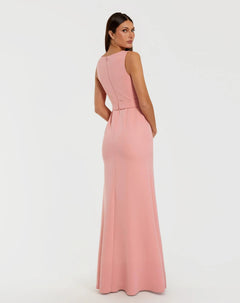 A woman is seen from behind, glancing over her left shoulder while wearing the Mac Duggal 50097 Long Formal Dress—a sleeveless, floor-length crepe gown in a light pink pastel shade—set against a plain white background.