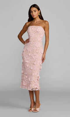 A woman wearing the Mac Duggal 50117 Midi Party Dress in blush, featuring strapless, 3D floral applique lace, paired with nude heels and standing against a plain gray background.