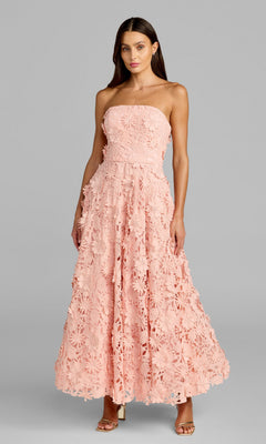 A woman stands against a plain gray background wearing the Mac Duggal 50118 Long Formal Dress in blush, featuring a strapless design with a floral textured pattern, paired with open-toe heels.