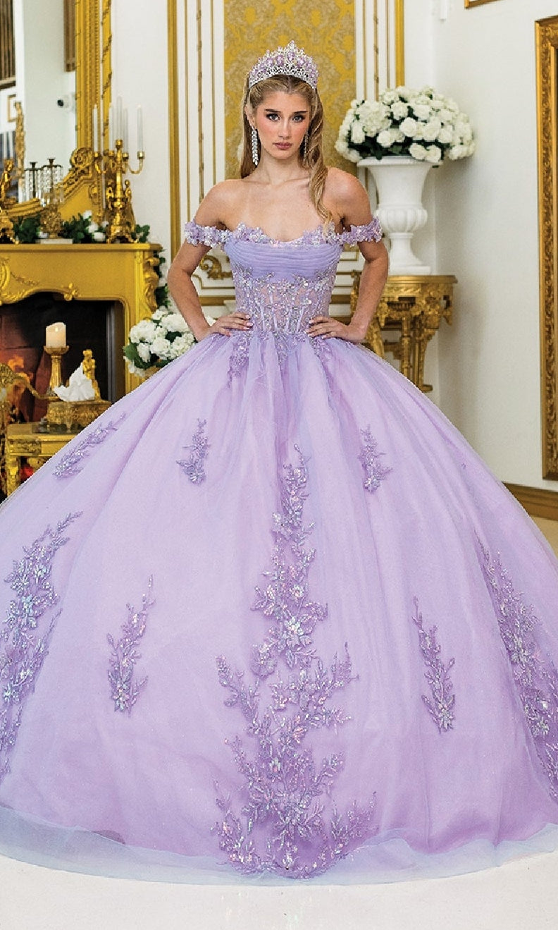A woman in the Lilac Quinceanera Dress 5011 By Dancing Queen, featuring a corset bodice and floral ball gown skirt, stands with a tiara in an ornate, gold-accented room filled with white flowers.