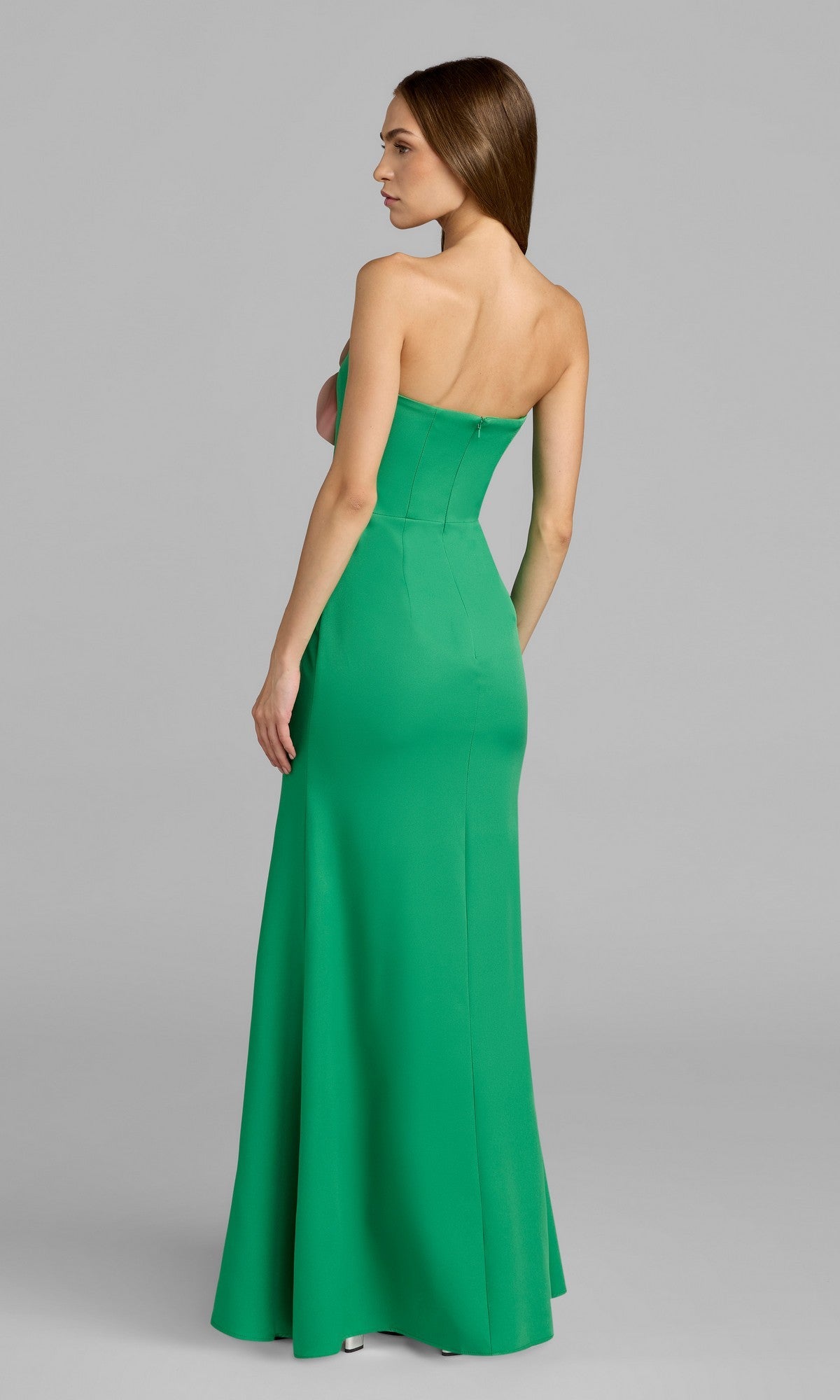 A woman stands sideways in the Long Formal Dress: Mac Duggal 50122—a stunning green, strapless, floor-length gown—set against a plain gray background.