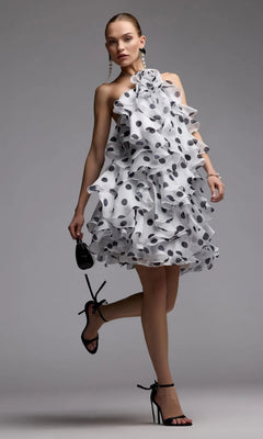 A woman poses in the Short Party Dress: Mac Duggal 50171—a chic polka dot halter dress with cascading ruffles—holding a small black purse and wearing black high-heeled sandals for an effortlessly elegant party look.