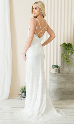 A woman wearing the Floral-Embellished Long Sequin Prom Dress 5020, a floor-length white gown with floral details and crisscross straps, stands indoors near decorative plants and light-colored walls.