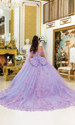 A woman in the Purple Quinceanera Dress 5029 By Dancing Queen, featuring a corset bodice and floral details, stands facing away in an ornate room with gold decor, a fireplace, and classical artwork.