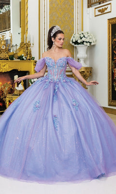 A woman wearing the Quinceanera Dress 5039 By Dancing Queen—a large, off-the-shoulder gown with a glitter tulle skirt and floral details—stands in an ornate, gold-decorated room with a tiara.