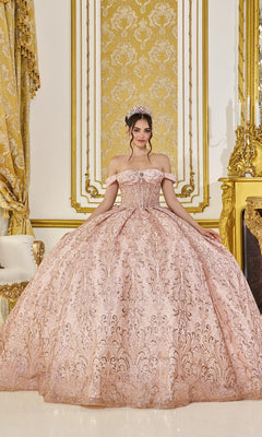 A young woman wearing the Quinceanera Dress 5043 By Dancing Queen in rose gold, featuring a corset bodice and ornate tulle skirt, stands in an opulent room adorned with gold accents, patterned drapes, and elaborate decor. A sparkling tiara completes her elegant look.