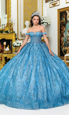 A woman wearing the Quinceanera Dress 5043 By Dancing Queen in Dusty Blue, featuring a sparkling tulle ballgown with a corset bodice and tiara, stands in an ornate room adorned with gold décor, flowers, and framed art.