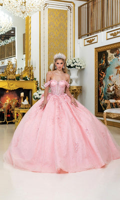 A woman in the "Quinceanera Dress 5056 By Dancing Queen" in blush, with a jeweled tiara, stands in an ornate gold-accented room featuring a fireplace and classical artwork.