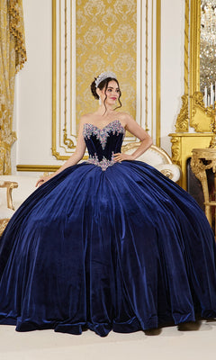 A woman wearing the Quinceanera Dress 5057 By Dancing Queen in navy with floral accents and a corset bodice stands in an ornate, gold-accented room, paired with a silver tiara.