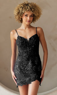 A woman wearing the Asymmetrical-Hem Short Homecoming Dress 5059S, a fitted black dress with sequin embellishments and thin straps, stands against a neutral background.