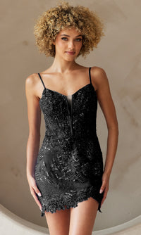 A woman wearing the Asymmetrical-Hem Short Homecoming Dress 5059S, a fitted black dress with sequin embellishments and thin straps, stands against a neutral background.