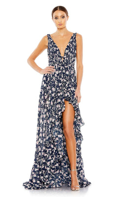 A woman models the Mac Duggal 50659 Floral-Print Maxi Party Dress—sleeveless, deep V-neck, navy blue with a ruffled high slit—paired with strappy heels, standing against a plain white background.