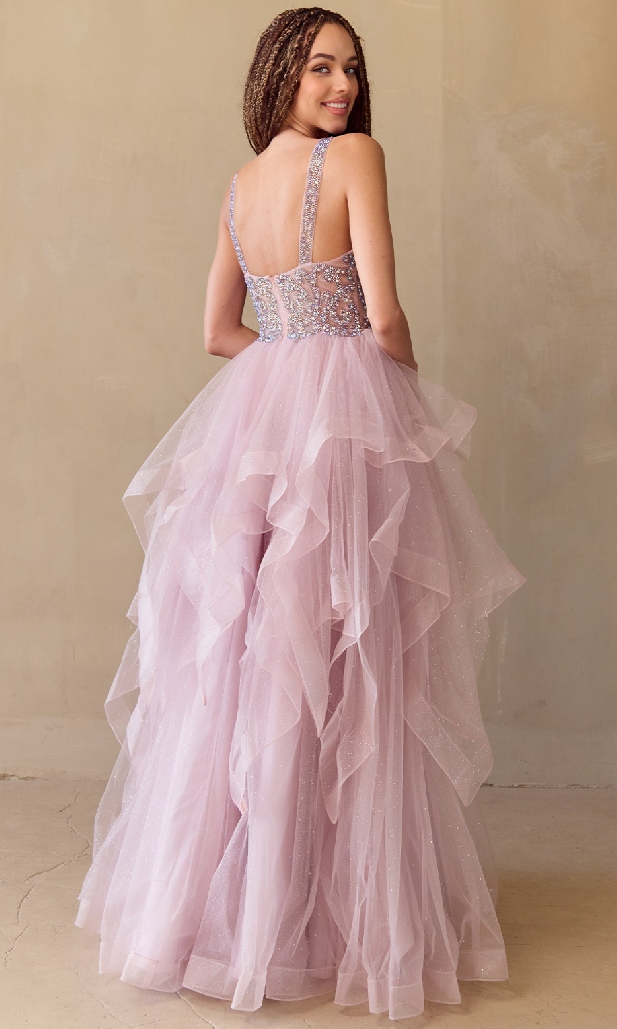 Woman modeling the back of a rose pink prom ball gown with a layered skirt in a beige room.